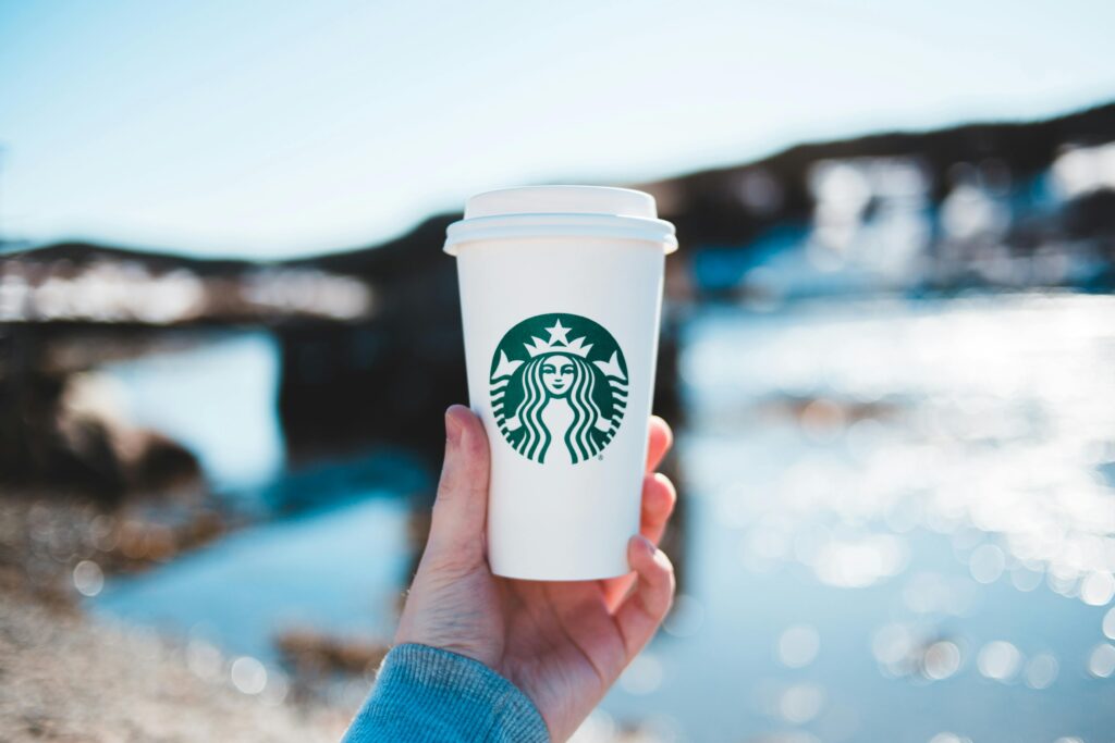 A person holds a Starbucks coffee cup with a scenic river view in the background.